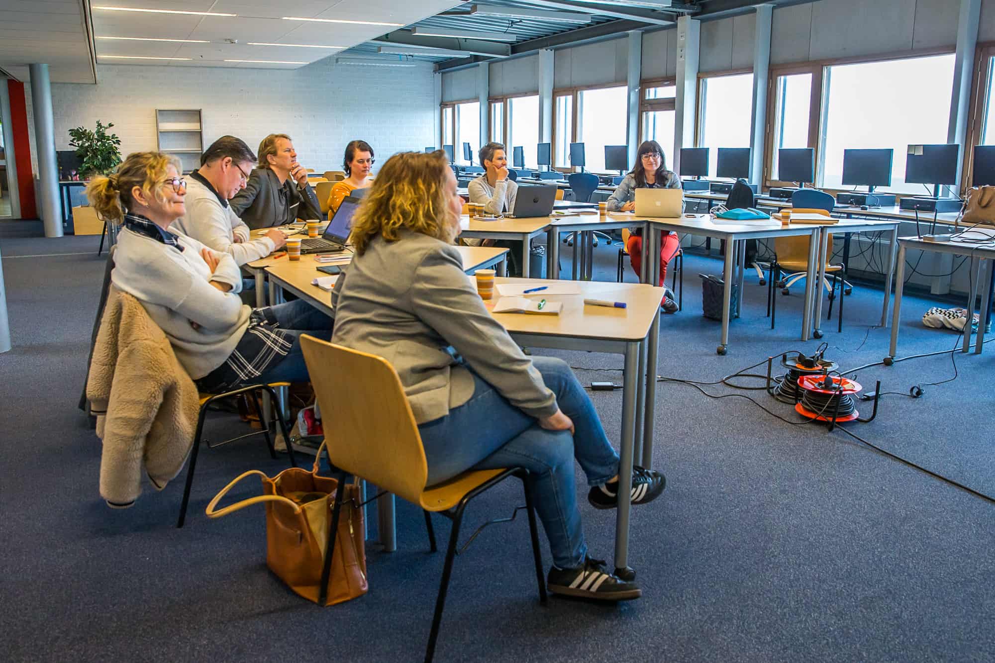 Foto van een luisterend groepje mensen, zittend achter tafels, achtergrondfoto op de pagina Onderwijs van mavadvieseninterim.nl