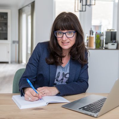 Portretfoto van Marja Verheijen, recht aankijkend en schrijvend in notitieboek, op de pagina Over mij van mavadvieseninterim.nl